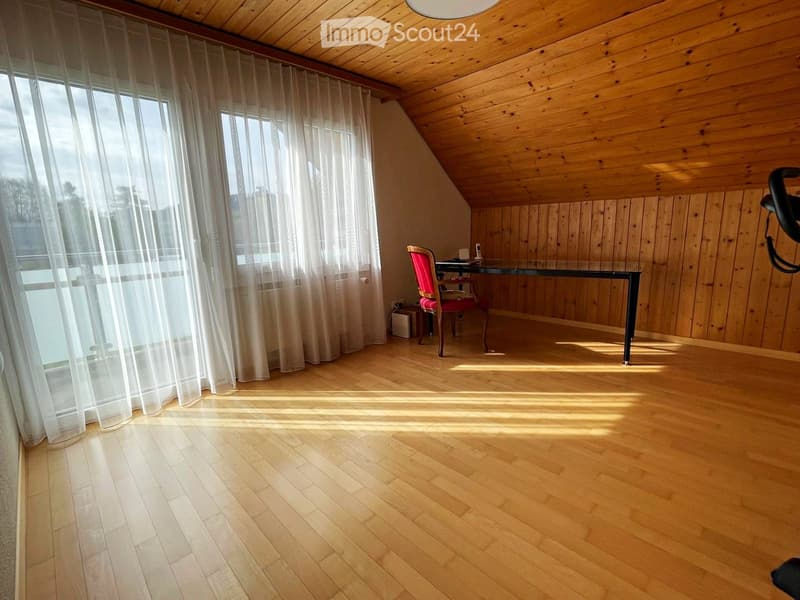 Bright, wooden-floored room with large windows and sheer curtains, featuring a single chair and table.