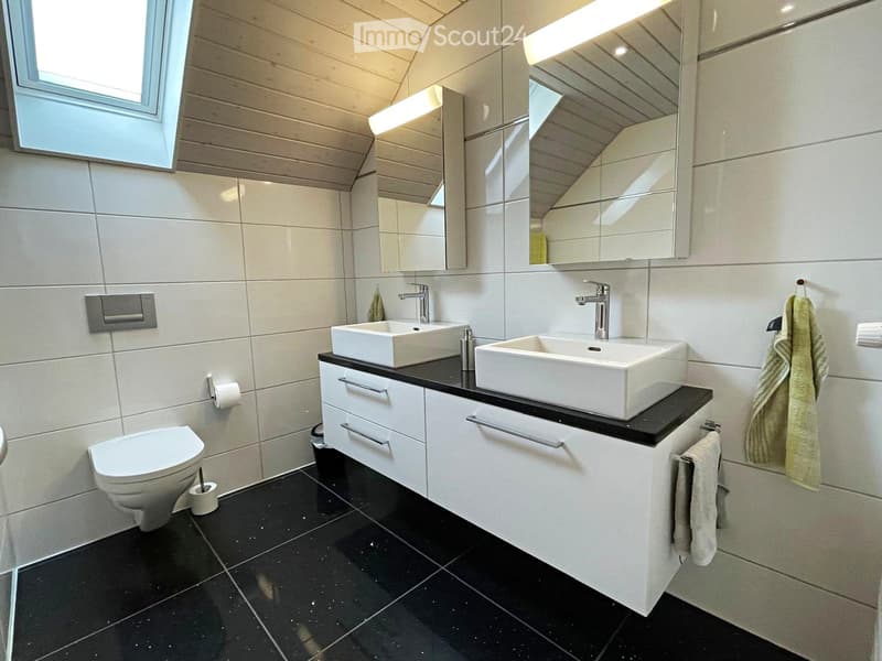 Modern bathroom with two white sinks, mirrored cabinet, black countertop, and white tiled walls.