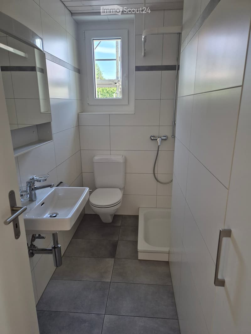 Modern bathroom with white tiles, a sink, toilet, bathtub, and a window providing natural light.