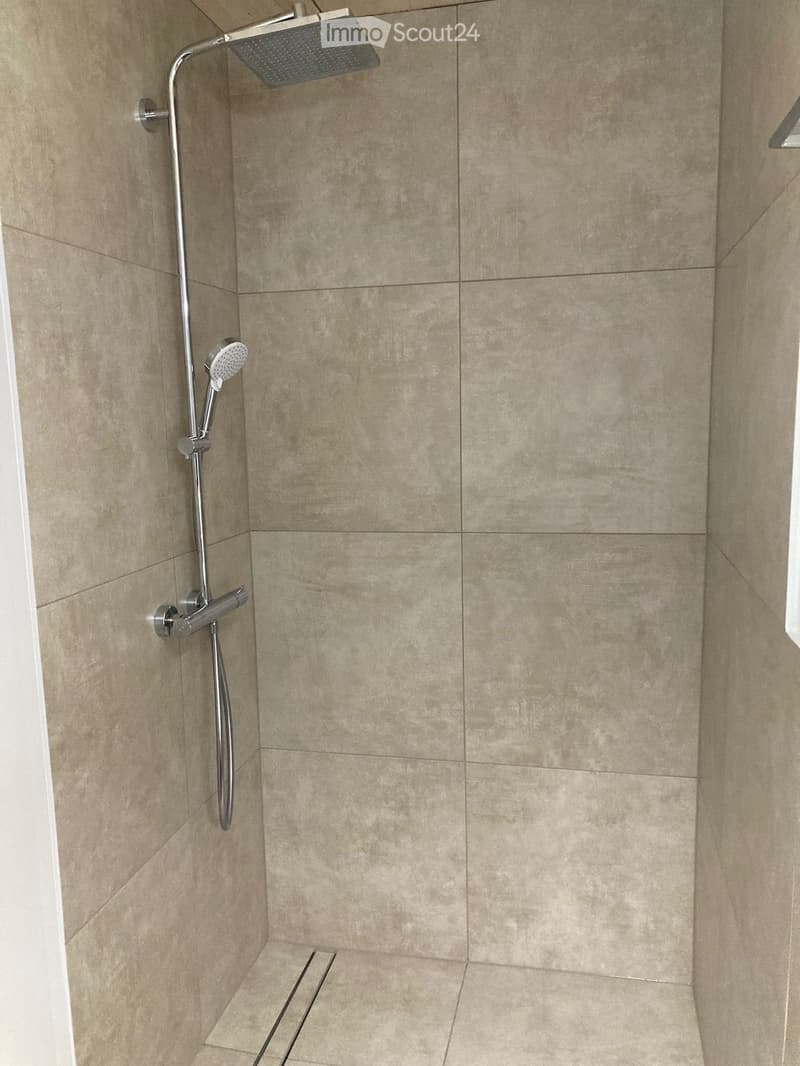 Modern shower area with beige tiled walls and floor, featuring a handheld showerhead and a fixed overhead showerhead.