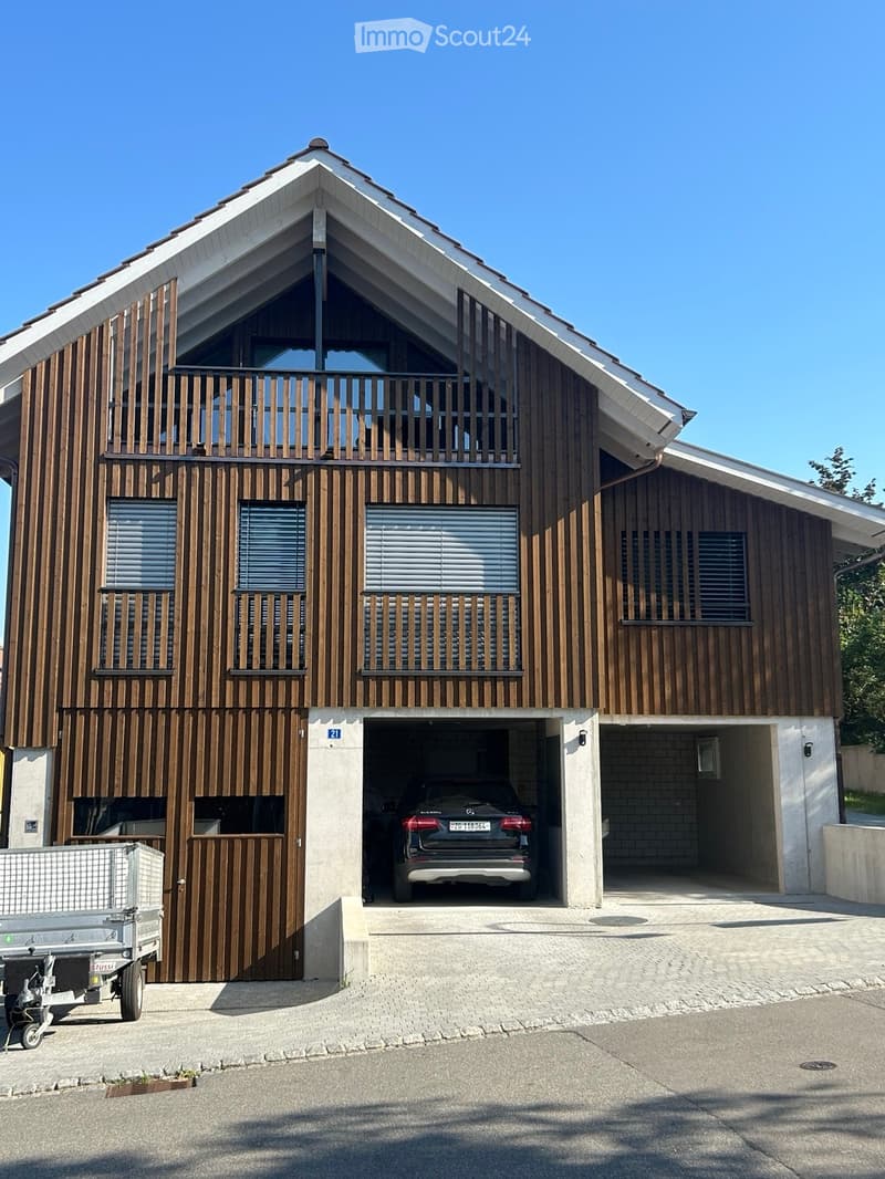 Modern two-story house with wooden facade, large garage, and balcony on the upper floor.