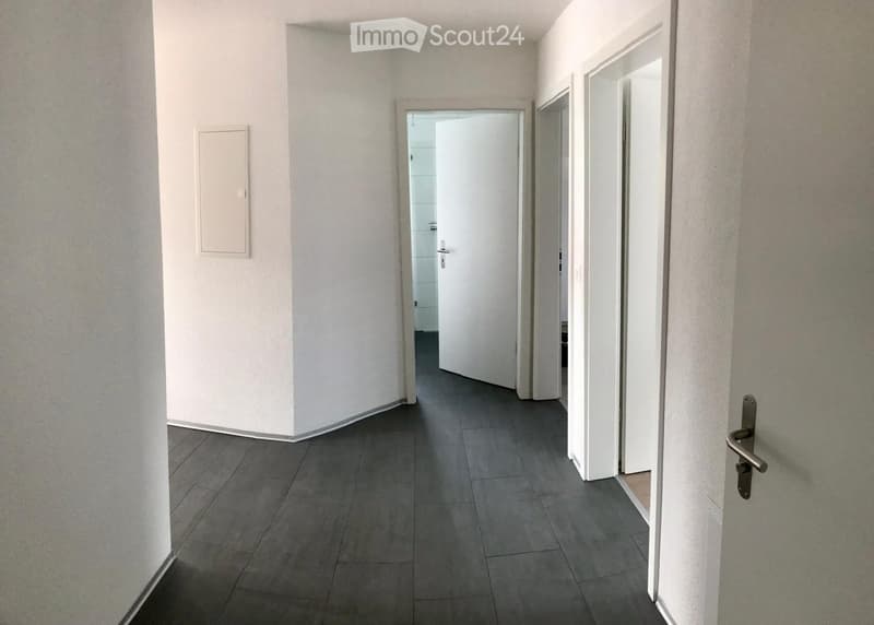 Empty hallway with grey tiled floor, white walls, and several doors leading to other rooms.