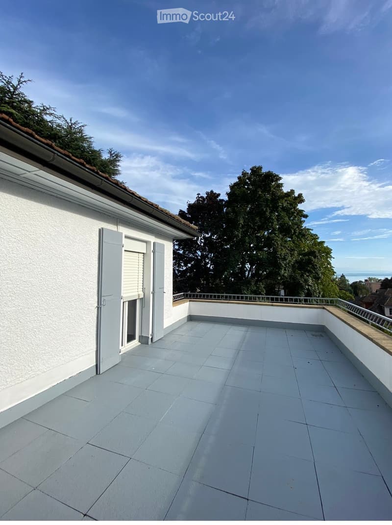 A clean, tiled balcony with white walls, a metal railing, and a door leading to the interior.