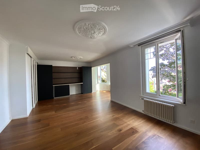 Empty room with wooden flooring, white walls, large windows, and built-in shelving unit.