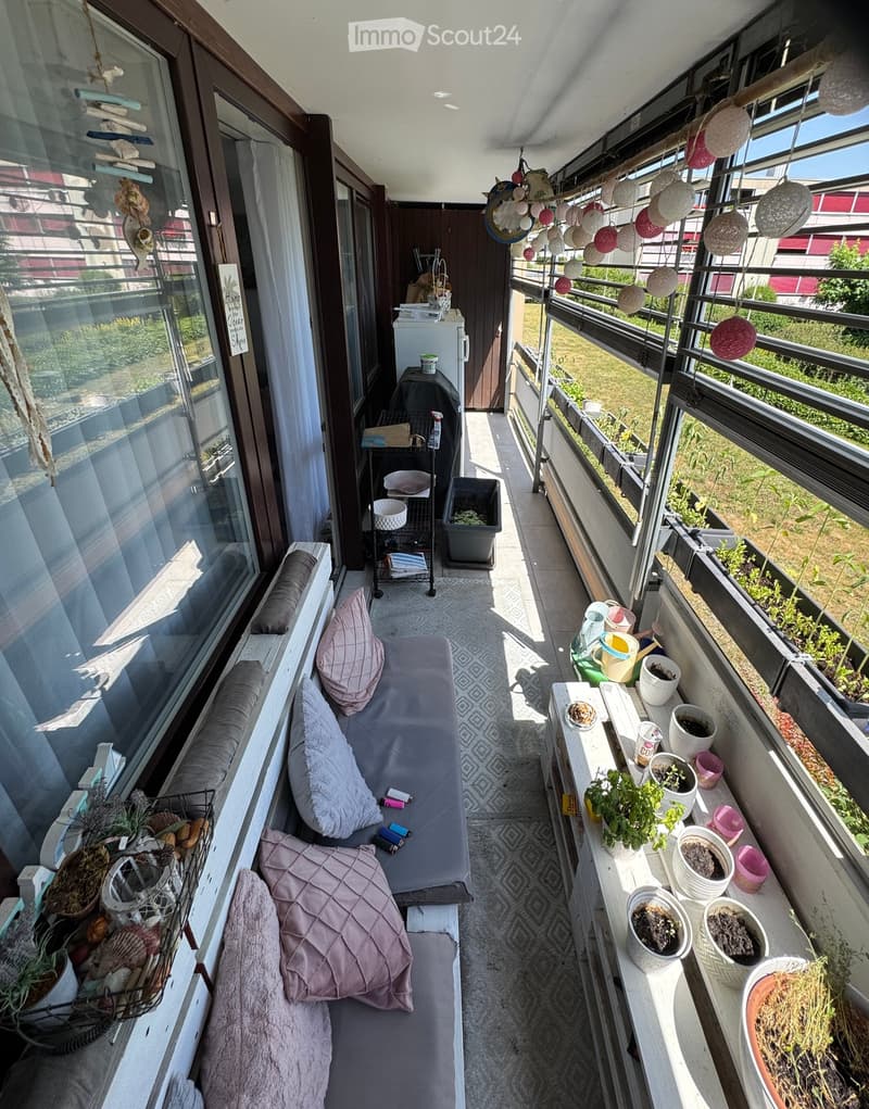 Balcony with a small seating area, cushions, potted plants, and hanging decorations.