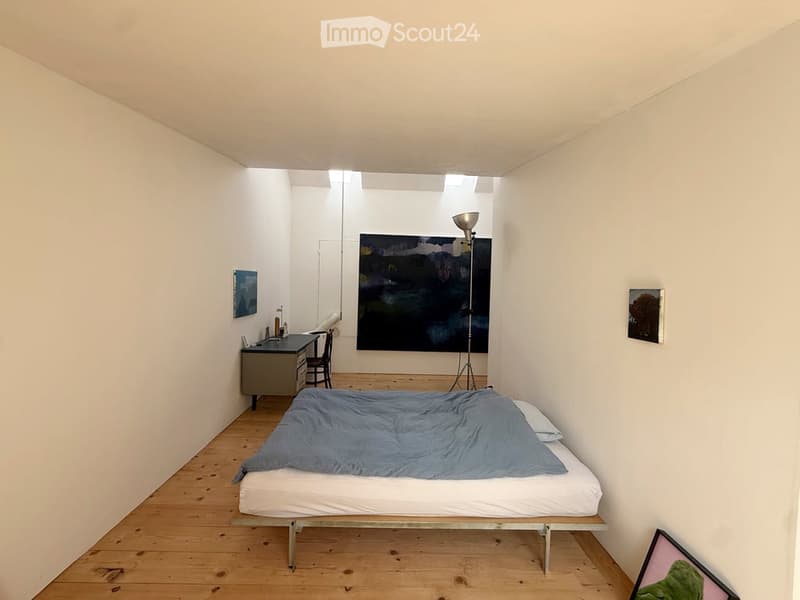Minimalist bedroom with a single bed, a desk, a chair, and artwork on the walls.