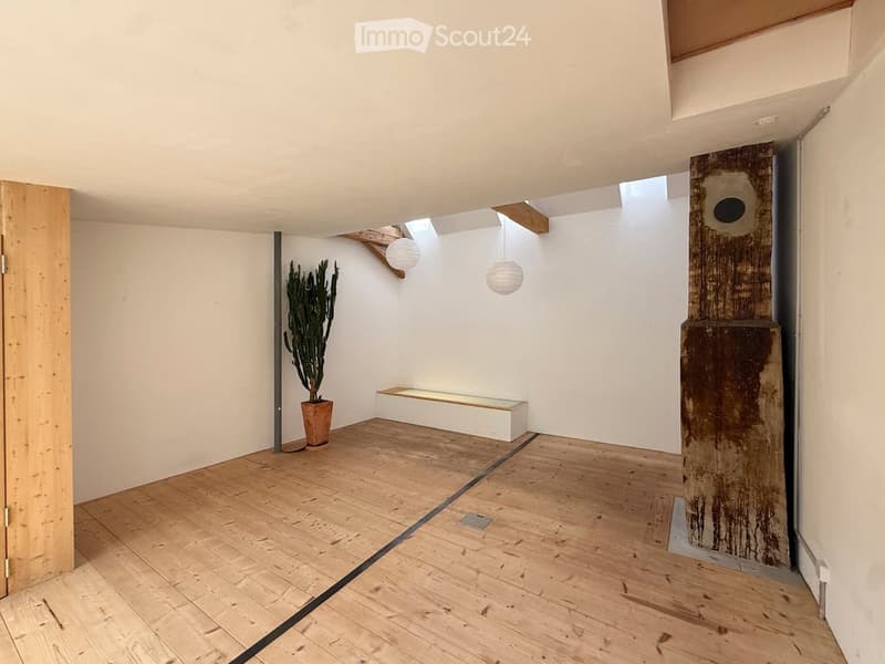 Empty room with wooden flooring, white walls, and a small built-in bench. A potted plant and pendant lights are present, but no furniture.