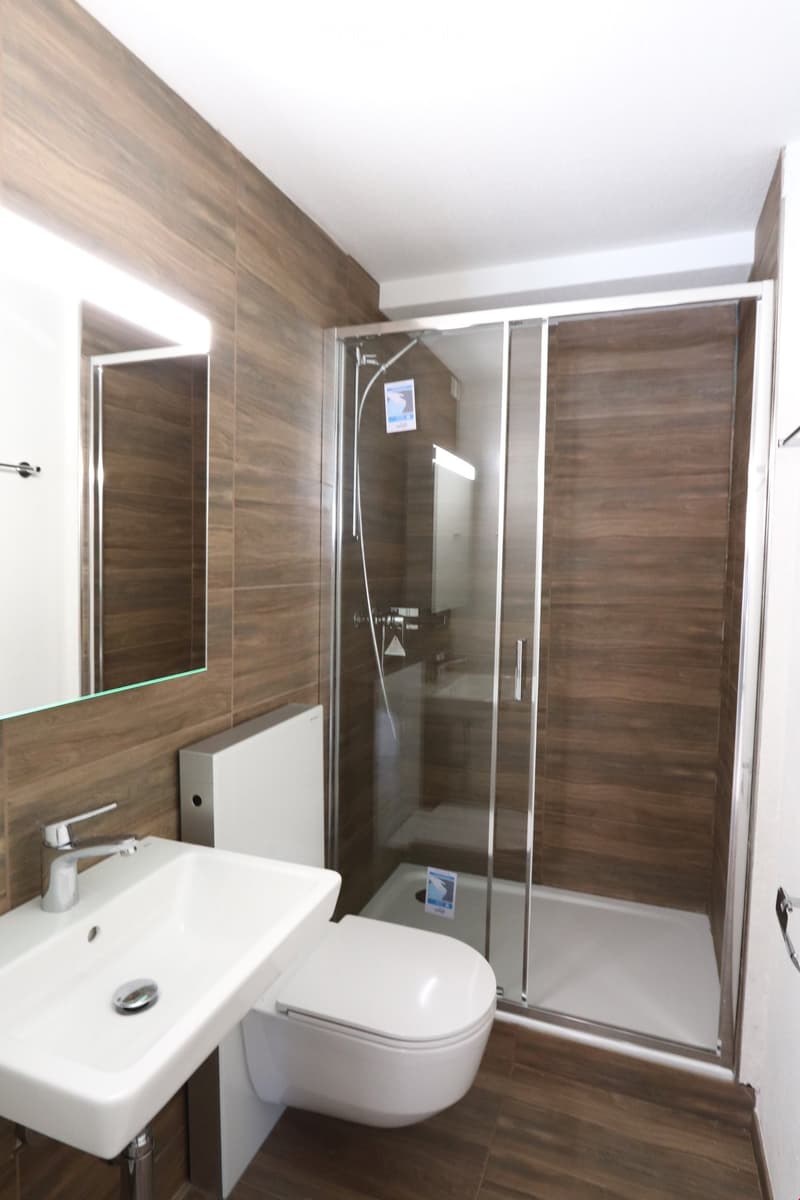 Modern bathroom with wooden walls, white sink, toilet, and glass-enclosed shower.