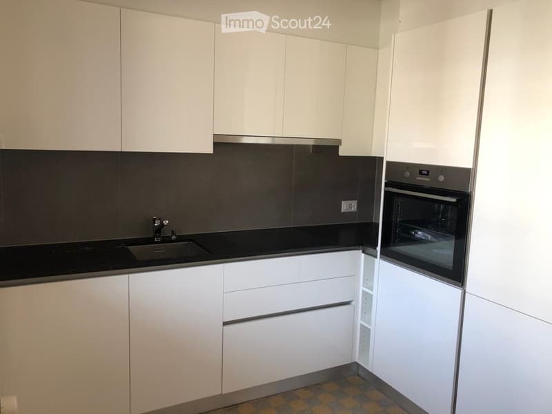 Modern kitchen with white cabinets, black countertops, and stainless steel appliances including a sink and oven.