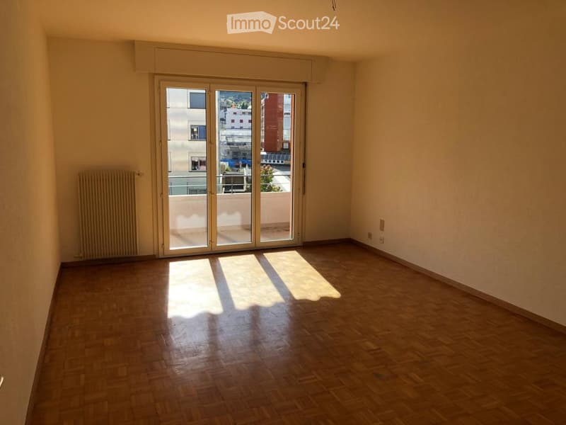 Empty room with wooden flooring, large sliding glass doors leading to a balcony with city view.