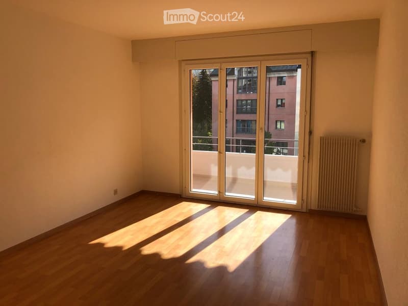 Empty room with wooden flooring, large glass sliding doors leading to a balcony, and a radiator on the wall.