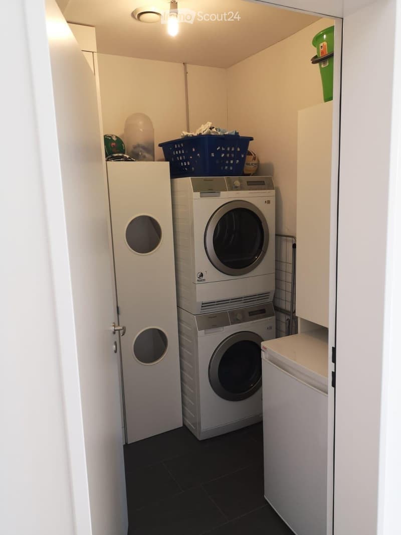 Compact laundry area with stacked washing machine and dryer, white cabinetry, and dark tiled floor.