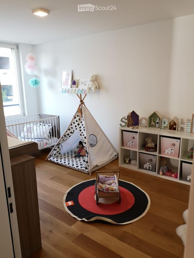 A well-lit children's bedroom with a crib, teepee tent, round rug, and shelves filled with toys and storage bins.
