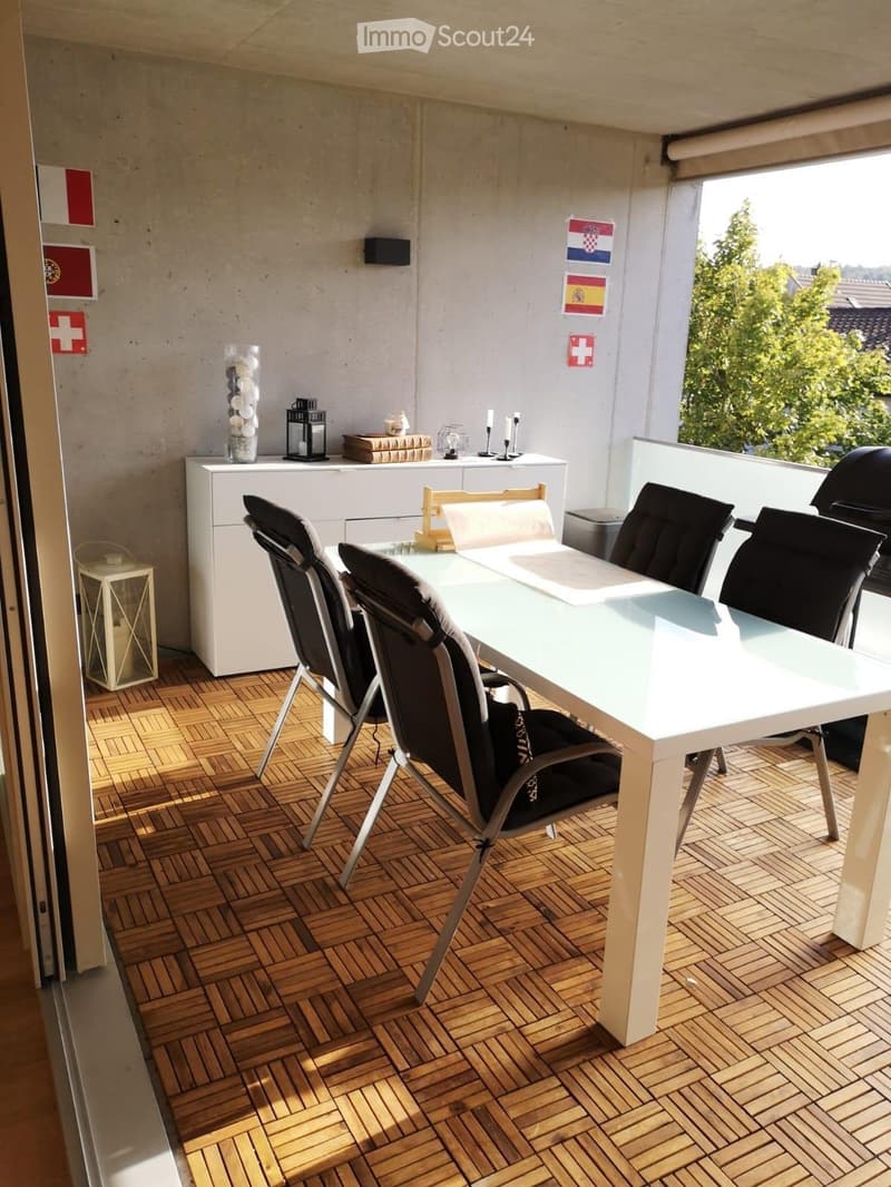 Balcony with wooden decking, white table and chairs, small cabinet, decorative lantern, and vase.