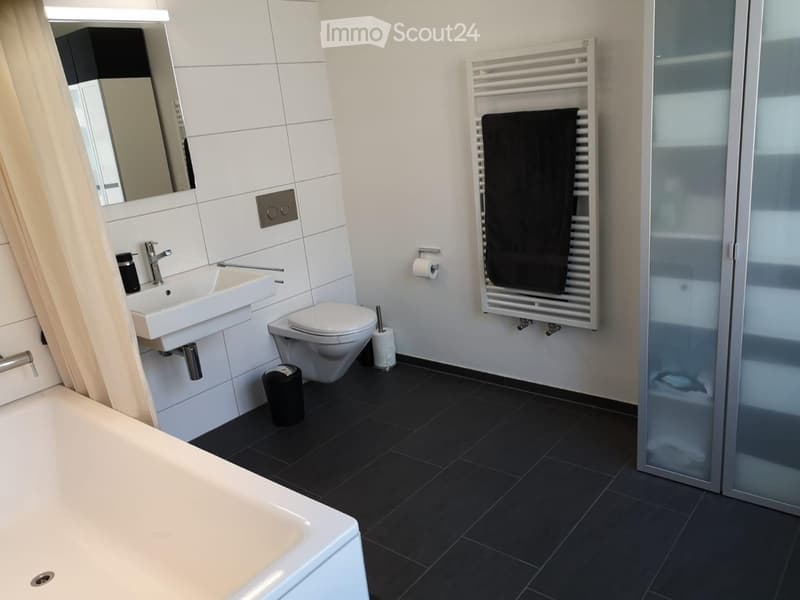 Modern bathroom with white tiles, black floor, bathtub, sink, toilet, mirror, towel rack, and towel.