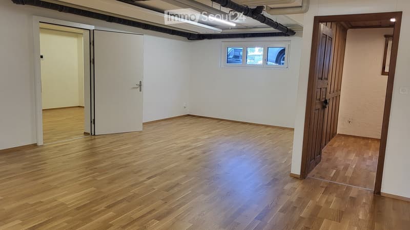 Empty room with wooden flooring, white walls, and two doors leading to adjacent spaces. A small window is visible on one wall.
