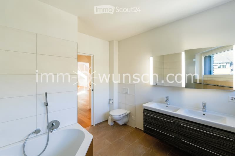 Modern bathroom with a bathtub, toilet, double sink, large mirror, and modern fixtures.