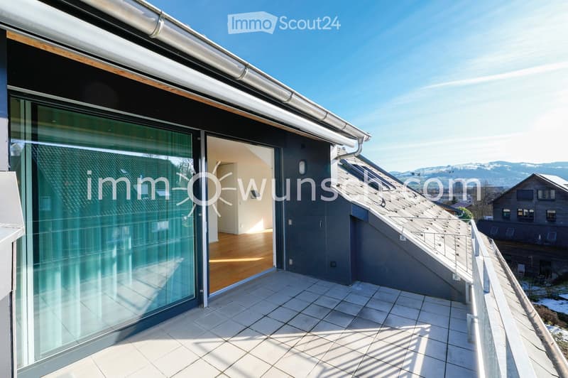 Modern rooftop terrace with tiled flooring, glass sliding doors leading to an interior space, and a panoramic view of surrounding mountains and houses.