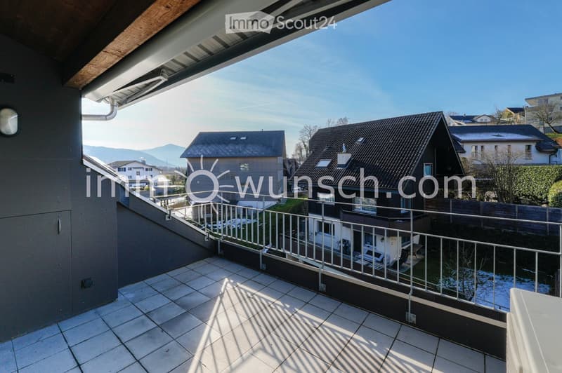 Balcony with tiled floor, metal railing, and a view of neighboring houses and mountains in the distance.