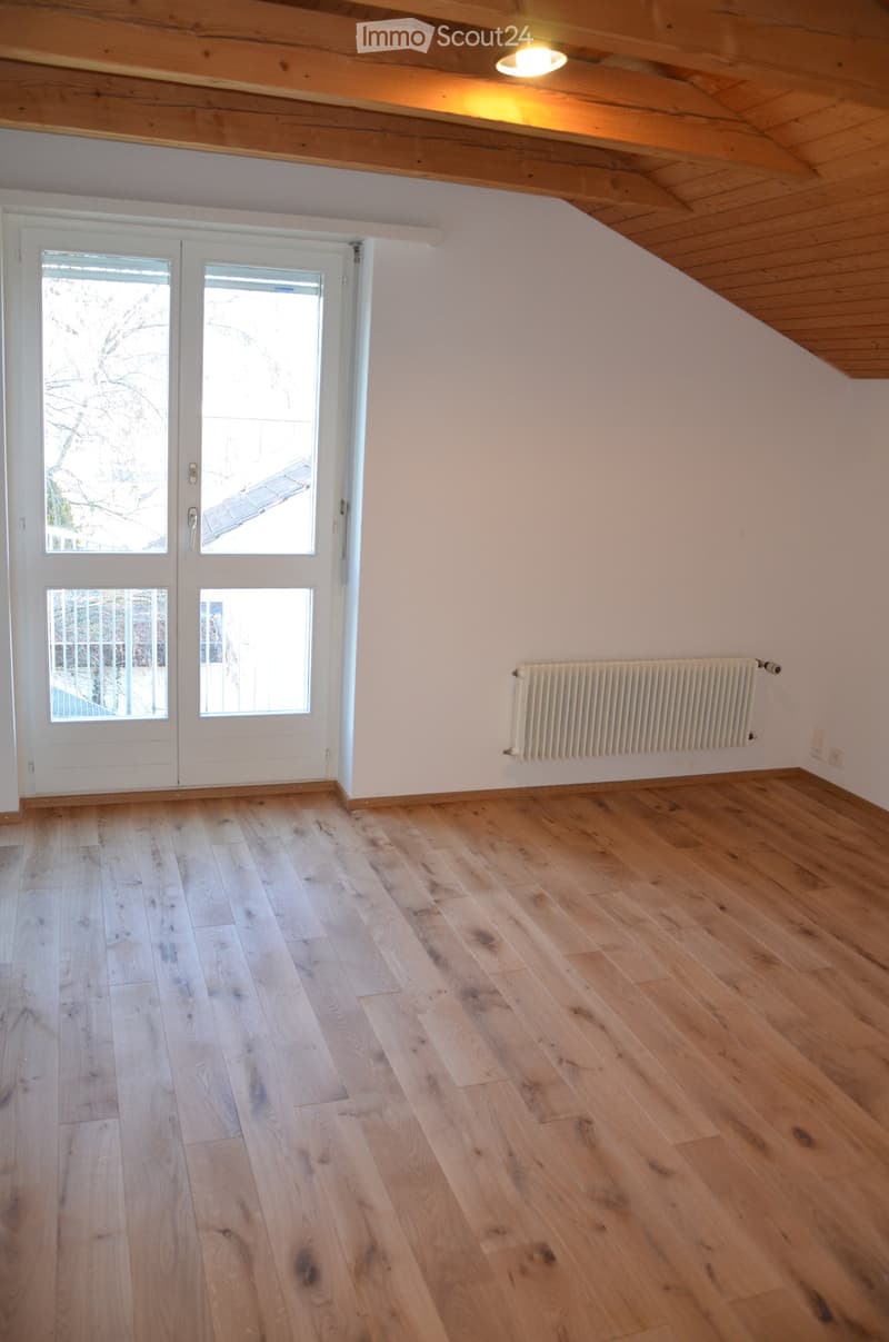 Empty room with wooden flooring, white walls, large double doors with glass panels, and a radiator on one wall.