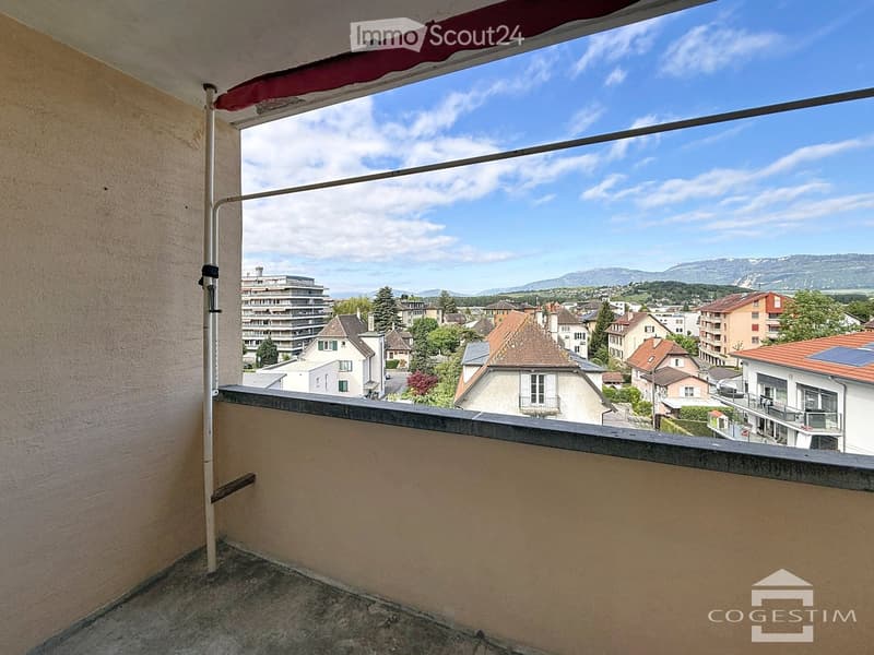 Balcony with a view of a town and mountains under a partly cloudy sky.