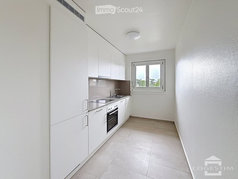 Modern kitchen with white cabinets, stainless steel sink, oven, and a window overlooking greenery.