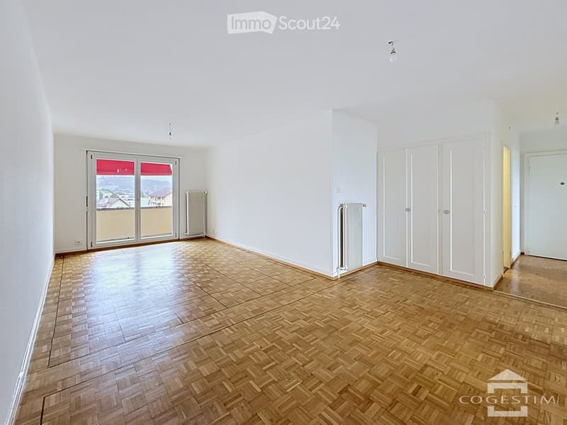Empty room with wooden herringbone flooring, white walls, large sliding glass door with red blinds, radiators, and built-in wardrobes.