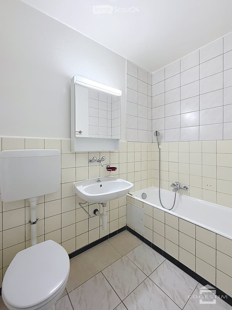 Modern bathroom with white tiles, a toilet, a sink, a bathtub, and a mirror cabinet.