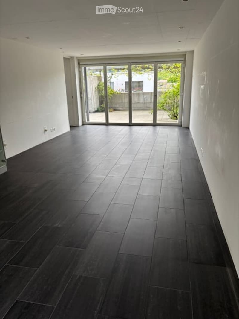 Completely empty room with dark wooden flooring, white walls, and large glass sliding doors leading to an outdoor area.