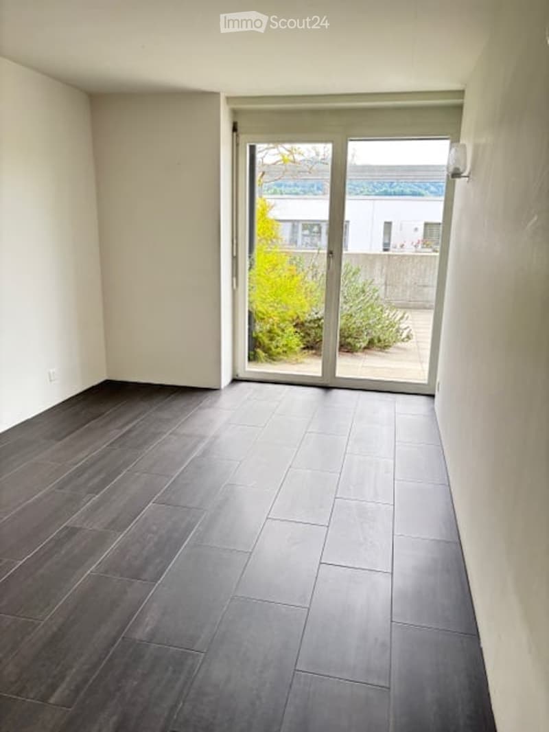 Empty room with dark grey tiled floor and large sliding glass door leading to outdoor area.