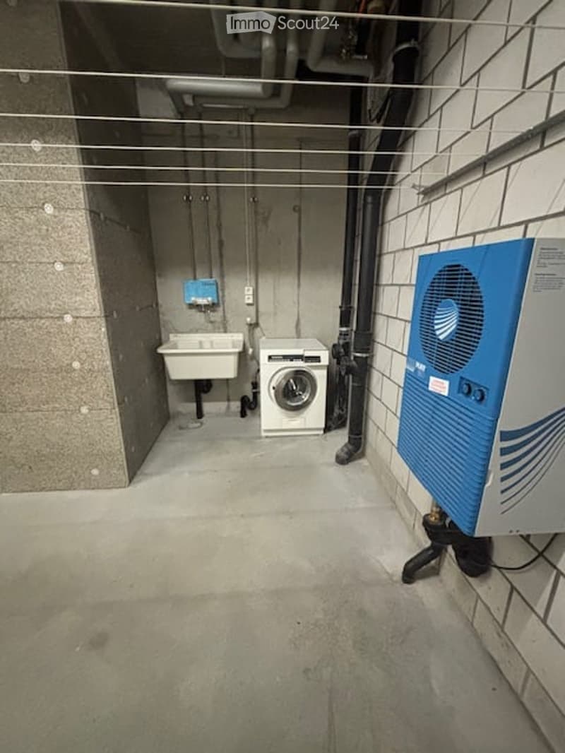 Utility room with a washing machine, sink, exposed pipes, and a water heater unit.