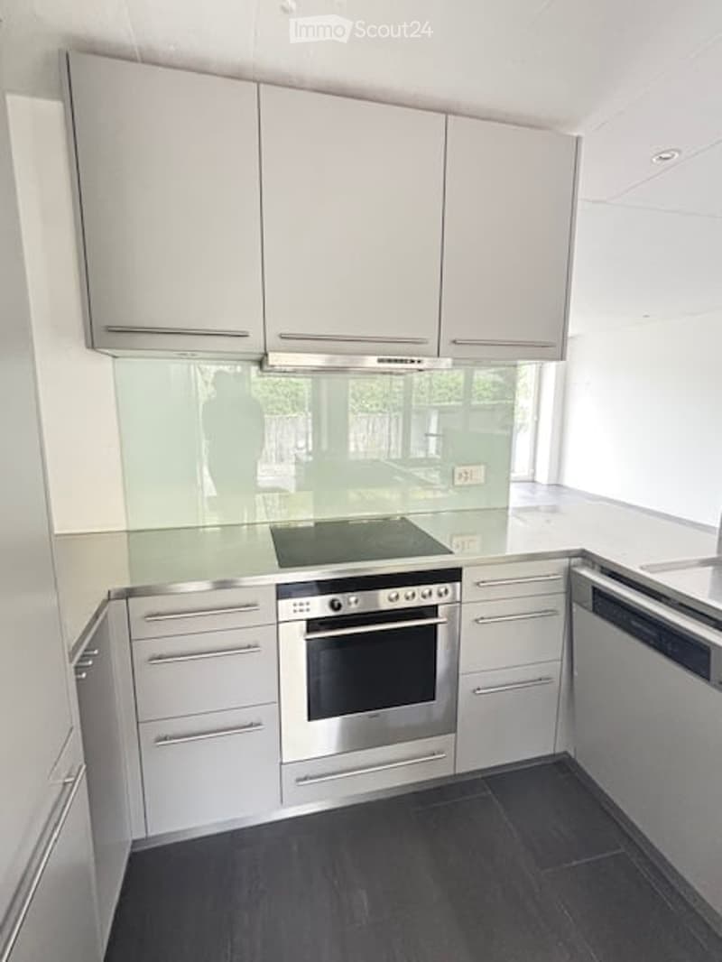 Modern kitchen with white cabinets, stainless steel appliances, and a dark tiled floor.