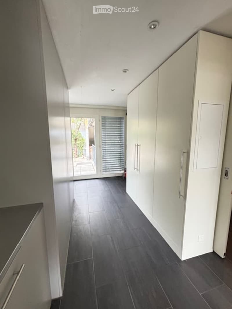 Modern hallway with dark tiled flooring, white walls, built-in white storage units with silver handles, and large glass doors leading to an outdoor area.