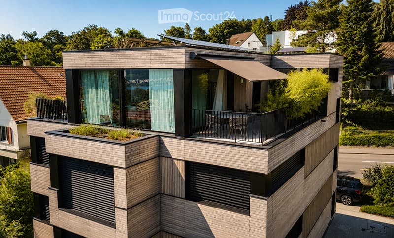 Modern two-story house with wooden facade, large windows, and a rooftop terrace with outdoor furniture and greenery.