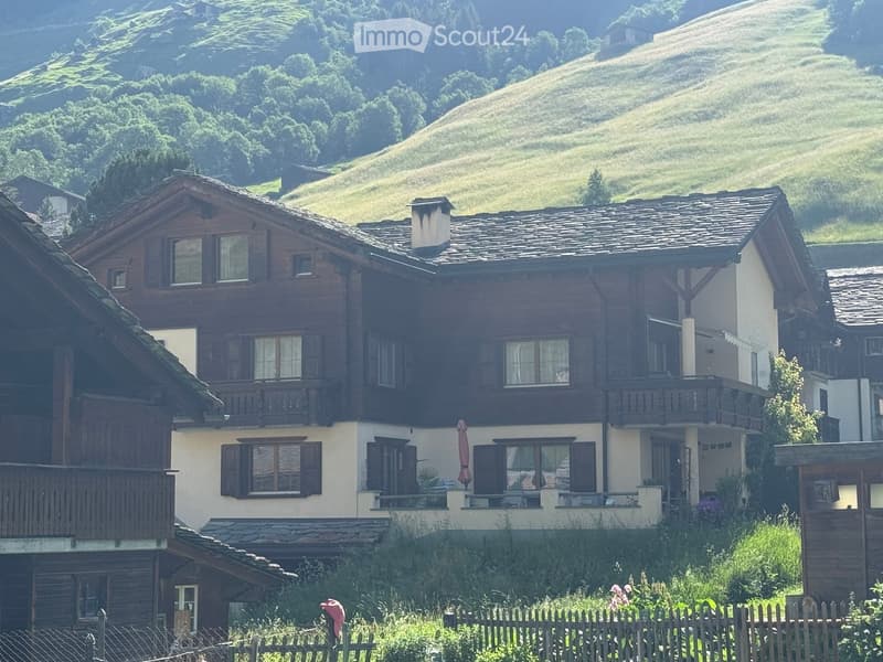 Traditional wooden chalet with multiple stories, stone and wood exterior, large windows, balconies, and a scenic mountain backdrop.