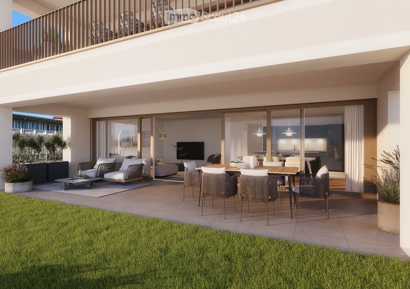 Modern outdoor patio with a sofa, coffee table, dining table, chairs, and a television visible through large glass doors. The space features a tiled floor, potted plants, and a grassy area.