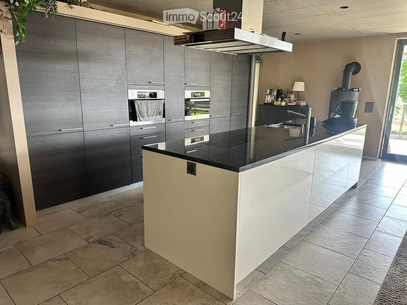 Modern kitchen with grey cabinets, black countertop, built-in oven, coffee maker, and a small table lamp on the counter.