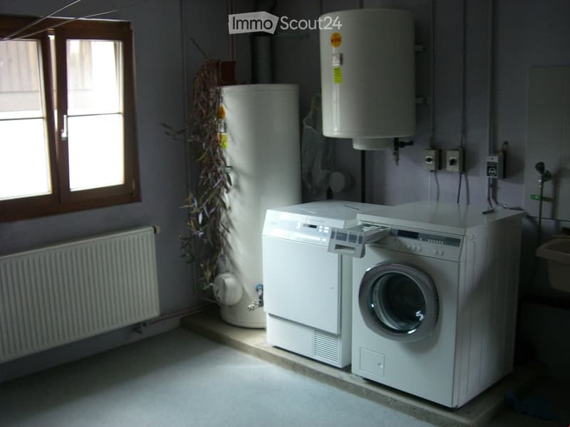 Utility room with a washing machine, water heater, and a window with wooden frame.