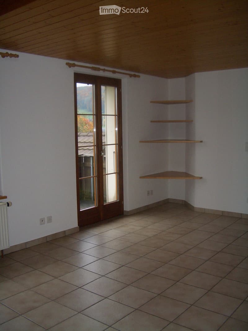 Empty room with tiled floor, white walls, wooden shelves, and a glass door leading outside.