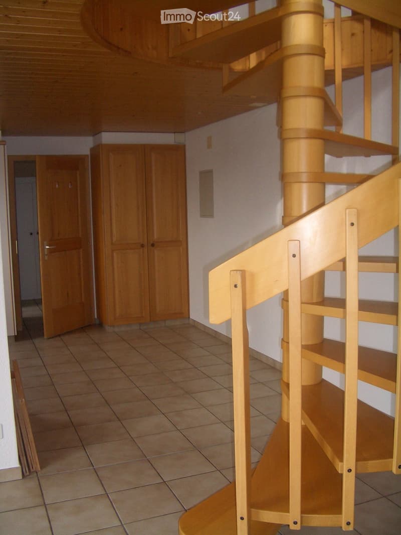 Empty hallway with tiled floor, wooden staircase, and closed wooden cabinet.