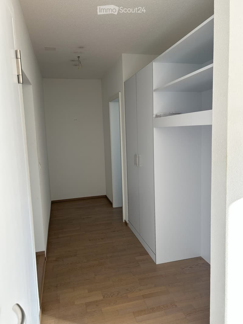 Corridor / Hallway. Empty hallway with wooden flooring, white walls, and built-in white shelving unit on one side.
