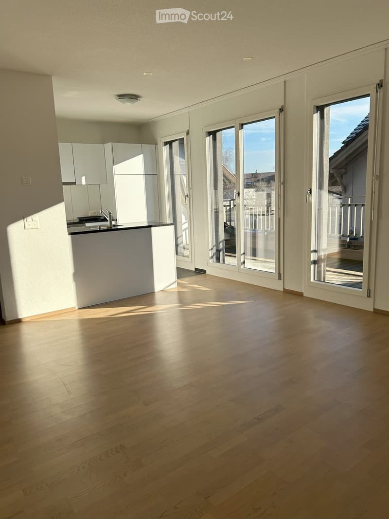 Unfurnished Room. Empty room with light wooden flooring, white walls, and large glass doors leading to a balcony area. Minimalist design with built-in cabinets and a small kitchen counter visible.