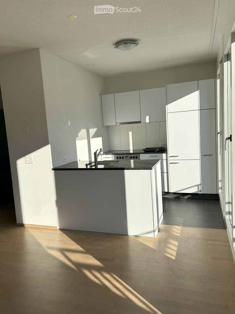 Kitchen. Modern kitchen with white cabinets, a central island, and a sink with a faucet. The floor is wooden, and the space is well-lit with natural light coming through a large window.