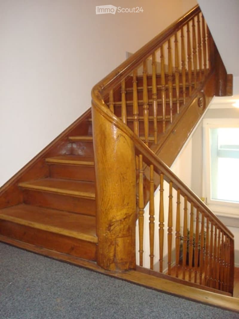 Corridor / Hallway. Spiral wooden staircase with polished steps and handrail, leading upwards in a well-lit interior space.