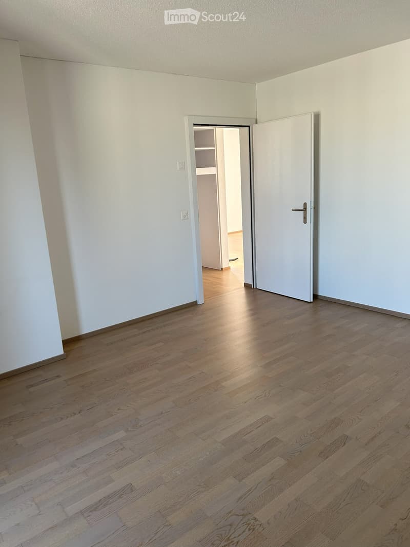 Unfurnished Room. Empty room with light wooden flooring and white walls, featuring a closed white door and an open doorway leading to another room.