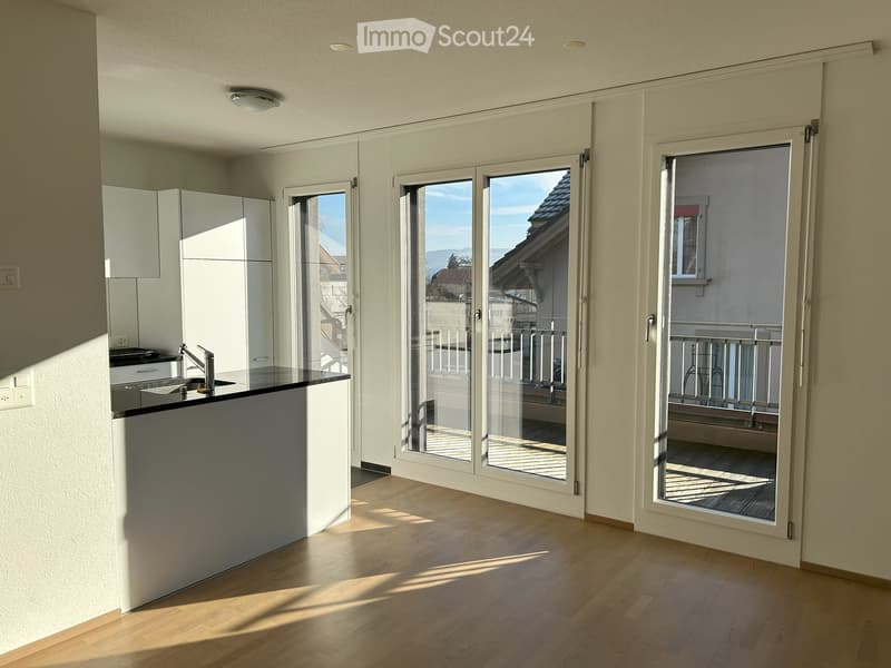 Furnished Room. Bright, modern kitchen with white cabinets, a black countertop, and a kitchen island. Large sliding glass doors open to a balcony with a view of the city.