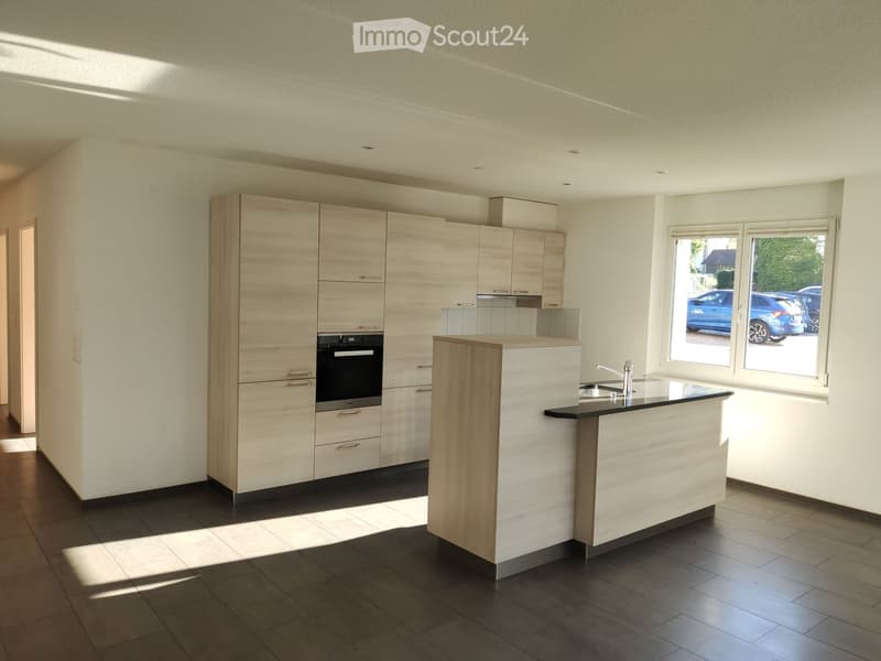 Modern kitchen with light wood cabinetry, stainless steel oven, island countertop, and sink.