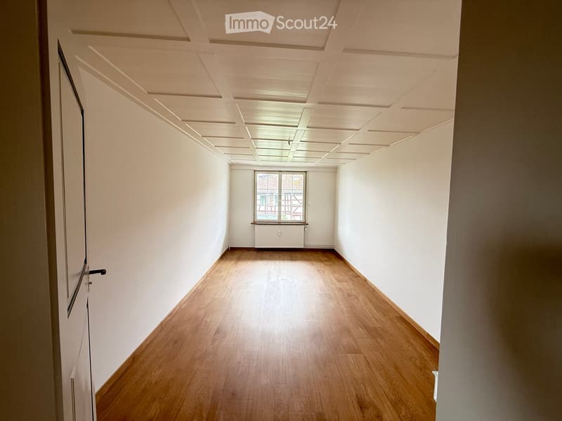 Empty hallway with wooden flooring, white walls, and a window at the end.