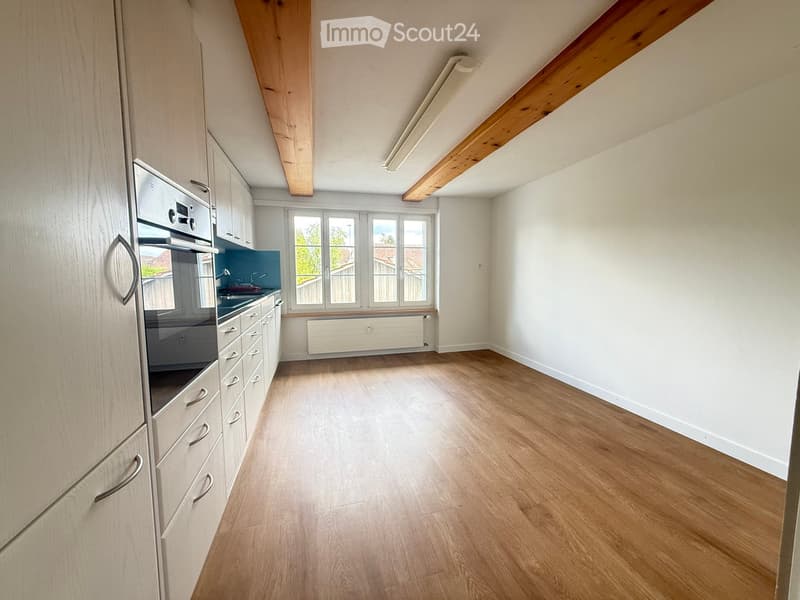 Empty kitchen with light wooden cabinets, stainless steel oven, and wooden flooring.