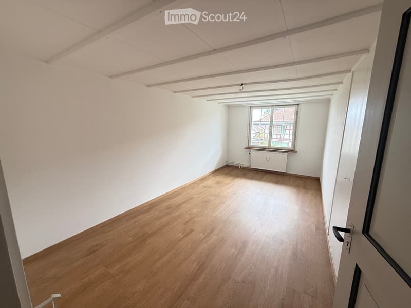 Empty room with wooden flooring, white walls, and a window with a view of the outside.
